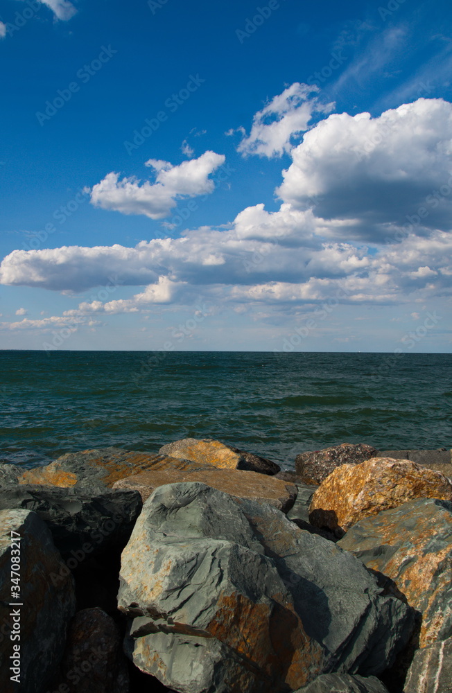 Romantic seaside landscape with grey and brown rocks, the green sea and the blue, cloudy sky on a sunny summer day Romantic seaside landscape with grey and brown rocks, the green sea and the blue, cloudy sky on a sunny summer day