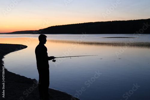 Man is fishing with a fishing rod on the river with orange-pink sunset photo