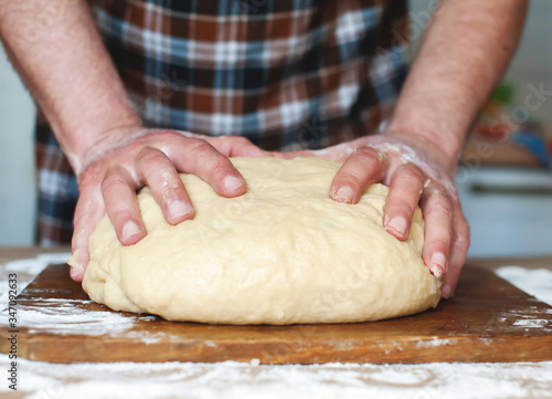 A man in an apron kneads the dough on a wooden board. Hands close up © Александр Довянский