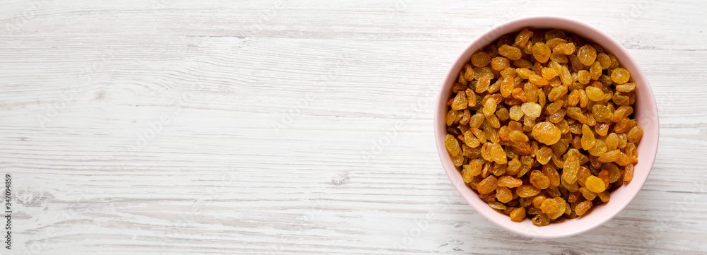Golden Raisins in a Pink Bowl on a white wooden surface, top view. Flat lay, overhead, from above. Space for text. Golden Raisins in a Pink Bowl on a white wooden surface, top view. Flat lay, overhead, from above. Space for text.
