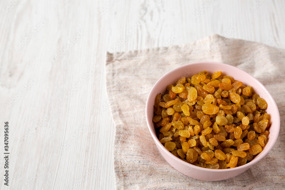 Golden Raisins in a Pink Bowl on a white wooden background, low angle view. Copy space. Golden Raisins in a Pink Bowl on a white wooden background, low angle view. Copy space.