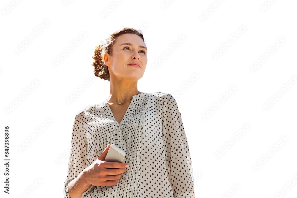 Cutout of young attractive woman holding smartphone while standing against office building with lens flare Cutout of young attractive woman holding smartphone while standing against office building with lens flare