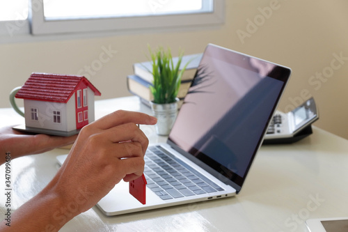 A man signs a contract to purchase a home with a real estate agent. Model house with keys on table.