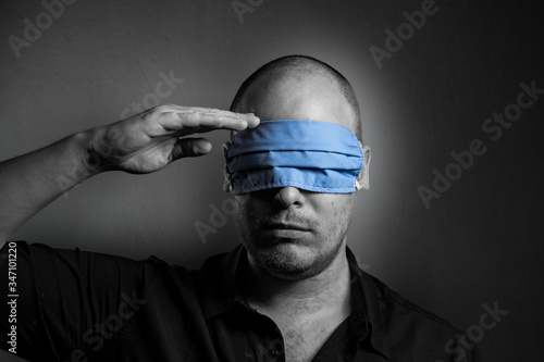 Mann hat mit MNS Maske die Augen verbunden und salutiert. Follow the Leader
