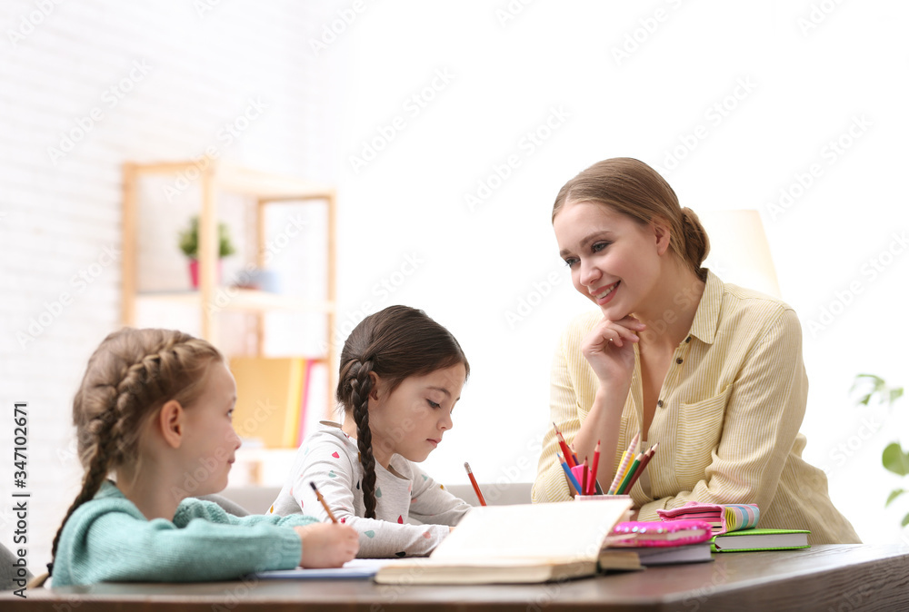 Mother helping her daughters with homework at table indoors Mother helping her daughters with homework at table indoors