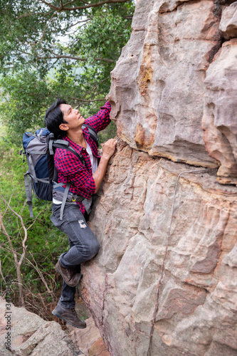 Backpacking male tourists trying to climb rocky cliffs