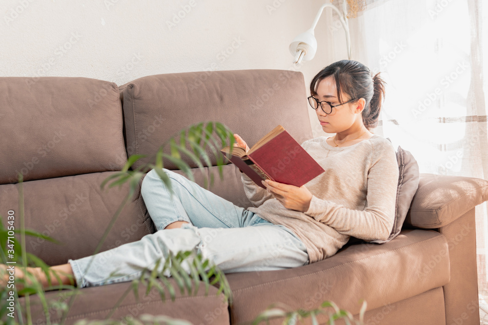 Asian woman relaxing at home reading an old book on the sofa. Girl enjoying quiet time indoors. lying on the couch. Asian woman relaxing at home reading an old book on the sofa. Girl enjoying quiet time indoors. lying on the couch.
