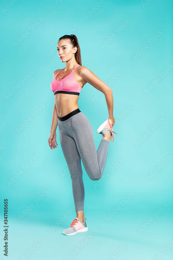 Stretching legs. Full length of young beautiful woman in sportswear warming up before workout while standing against blue background
