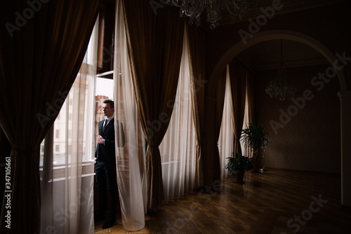in the large hall with huge windows stands the bride  dark curtains and high ceilings