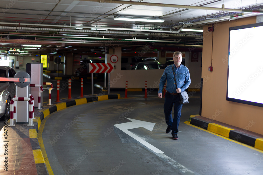 A man leaves the car parking. A 35-40 year old Caucasian man walks through an underground car park.