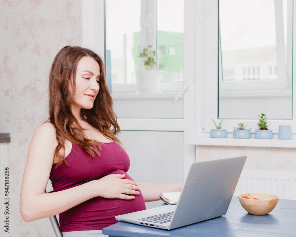 Pregnant young woman using a laptop computer. The concept of work from home or online learning. Stay home. Video calling.Selective focus on the stomach. Pregnant young woman using a laptop computer. The concept of work from home or online learning. Stay home. Video calling.Selective focus on the stomach.