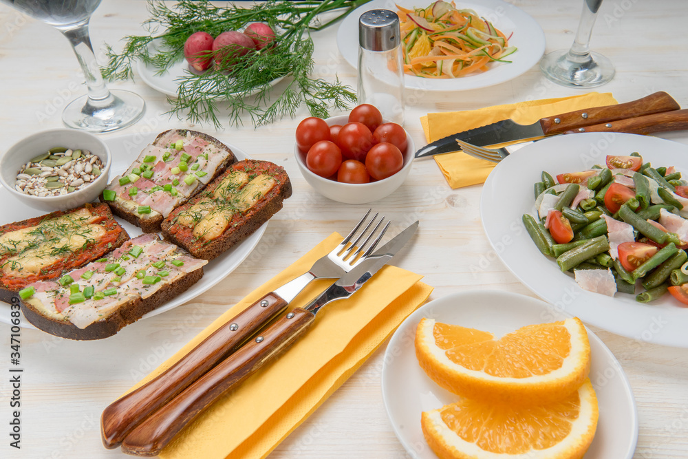 Waiting for lunch. Prepared salads of green beans, tomatoes, carrots, sandwiches with bacon cheese and herbs. Vitamin healthy snacks from cherry tomatoes, radishes, orange and cereals