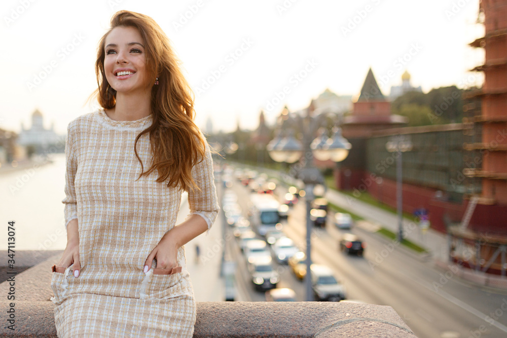 Beauty portrait of a stylish smiling red hair woman, touching her face, wear e in elegant dress standing on balcony.
