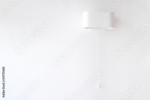 настенная белая лампа с кружком на белой стене со шнуром для включения и выключения