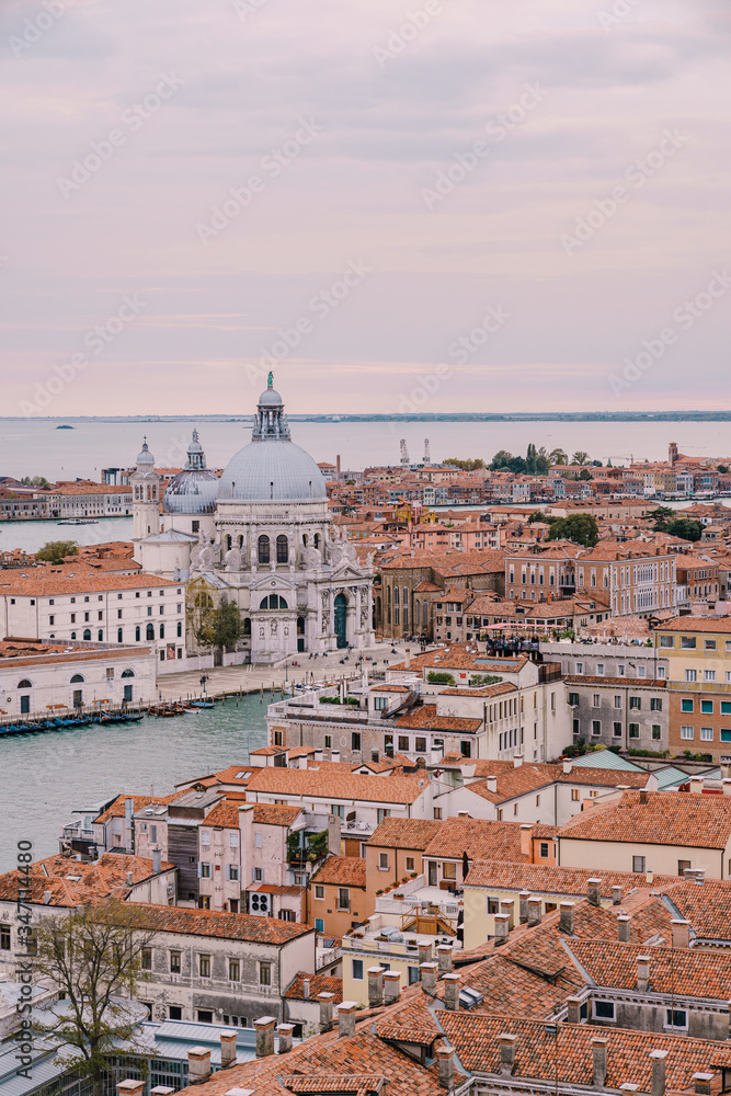 Aerial view from huge cathedral bell tower St Mark's Campanile on Santa Maria - Della - Salute - Church in the name of St. Mary the Savior, sunset sky and orange roof tiles. Venice, Italy 