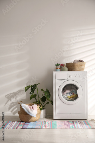 Modern washing machine and wicker basket with laundry near white wall. Interior design