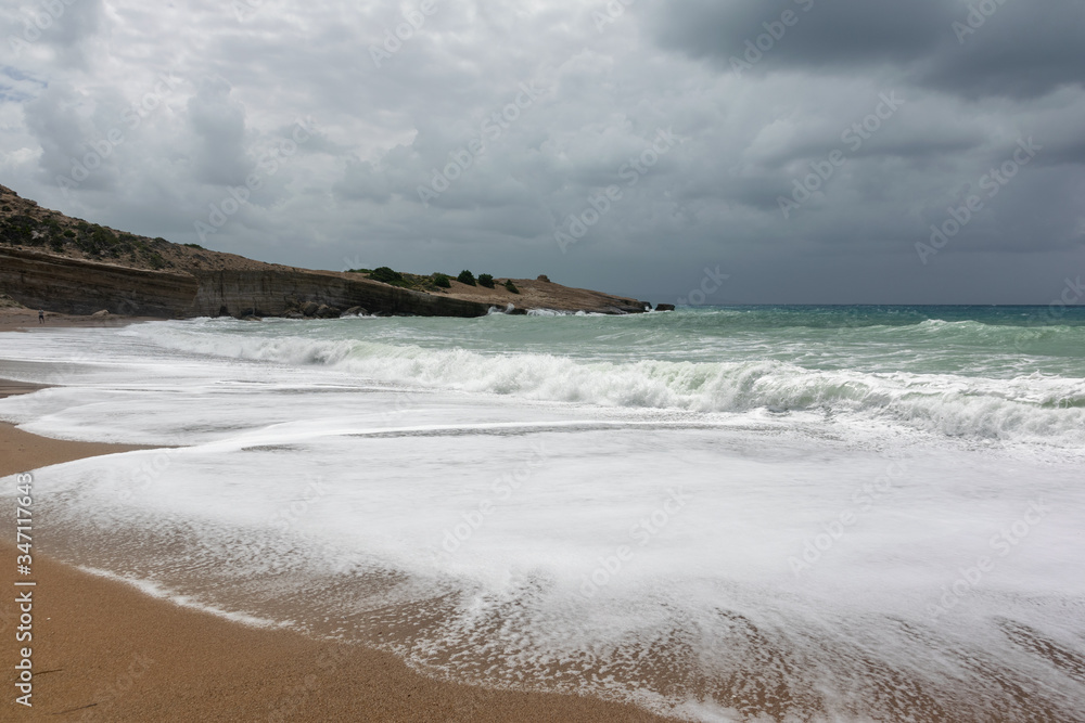 Dramatic rainy sky and stormy waves on a sand beach of the Aegean Sea in Rhodes.