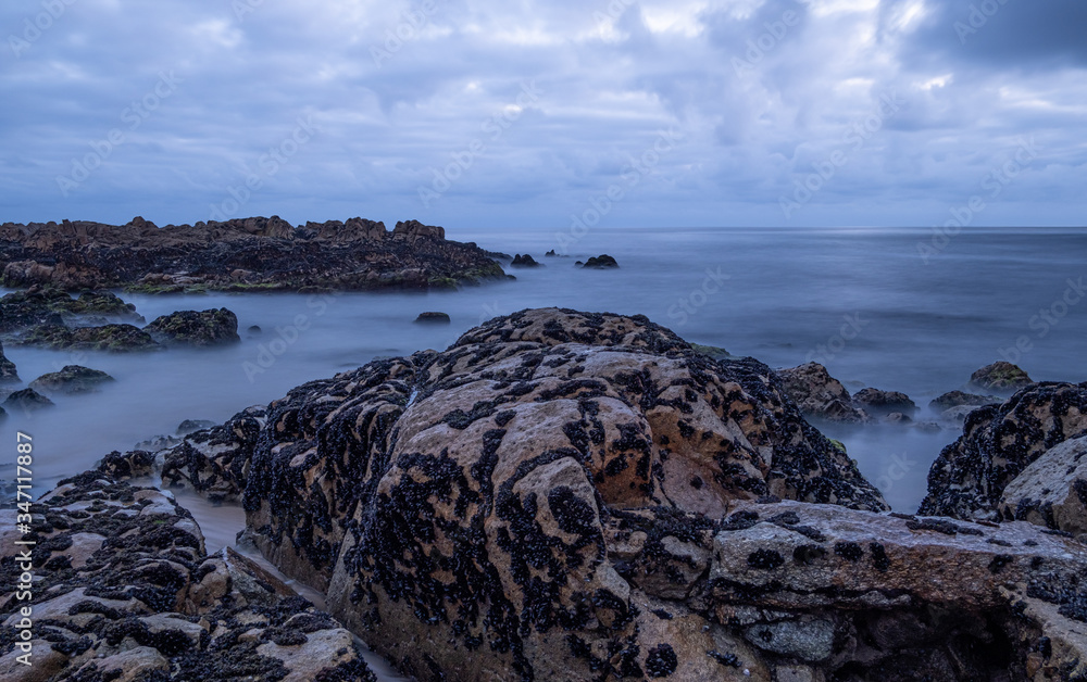 Long exposure shot of milky waves washing over rocks on the beach at dusk.