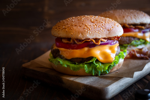 Burger with cheese, bacon, tomato and lettuce on dark wooden background