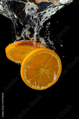 whole and sliced orange falling under water with a splash and bubbles on a white or black background