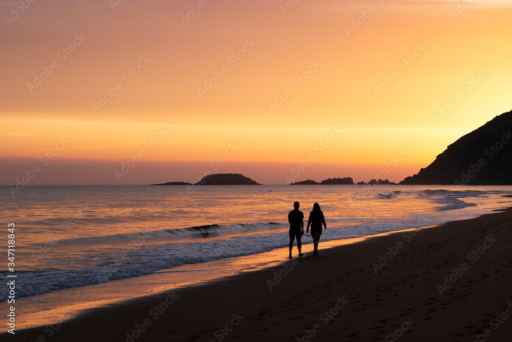 two people walking along the seashore in a beautiful orange sunrise