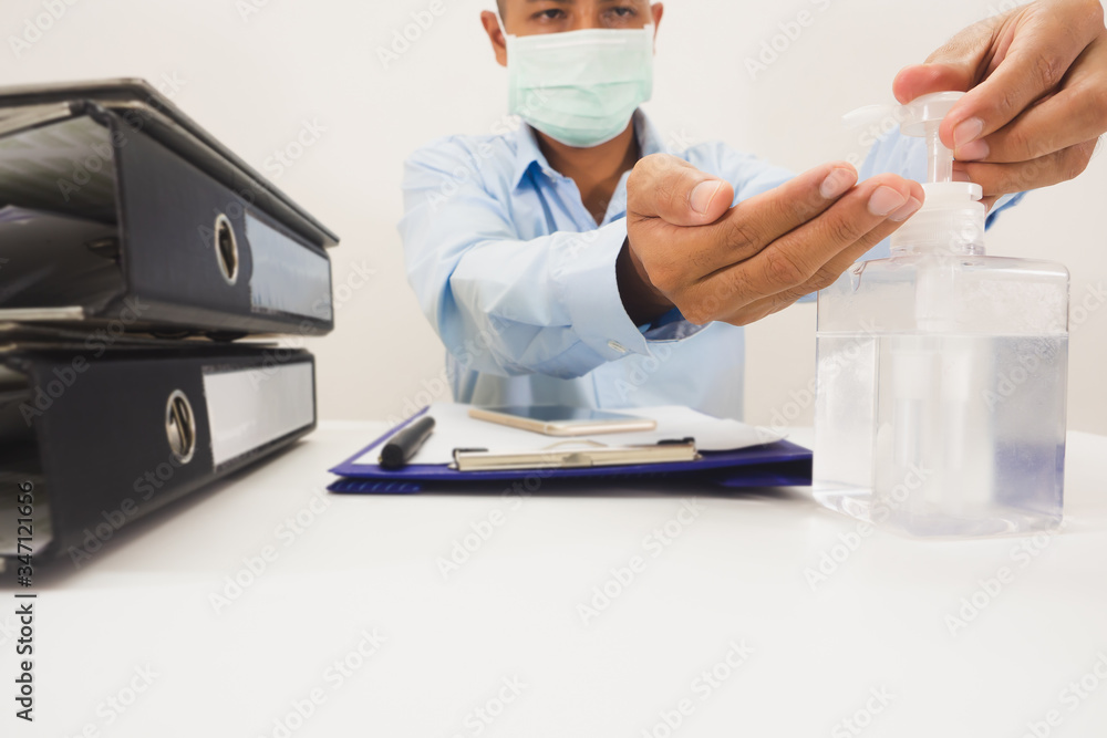 A white bottle of handwashing gel with the hands of a businessman sitting in a press to wash his hands before disinfecting work. On the desk, there were documents, phones, pens, taken from the front. A white bottle of handwashing gel with the hands of a businessman sitting in a press to wash his hands before disinfecting work. On the desk, there were documents, phones, pens, taken from the front.