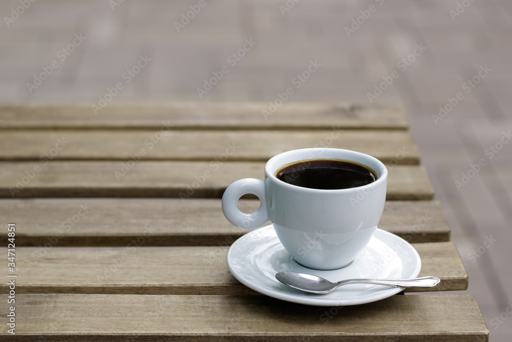 Coffee cup with tea spoon on wooden table on street Coffee cup with tea spoon on wooden table on street