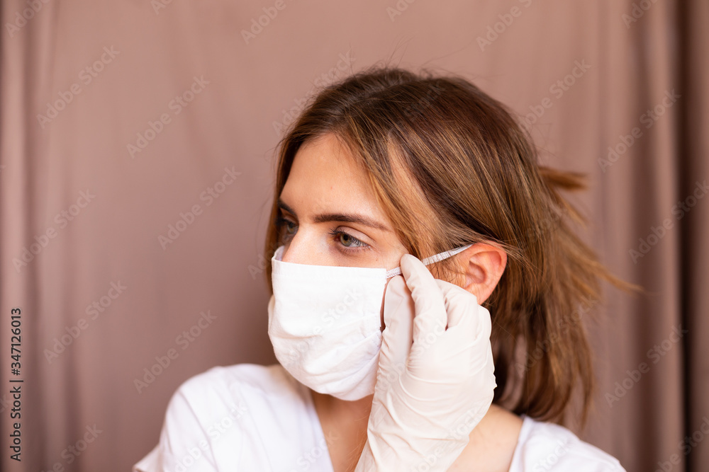 portrait of beautiful young woman wearing cotton white mask and medical/surgical gloves on pastel background. She is adjusting mask. portrait of beautiful young woman wearing cotton white mask and medical/surgical gloves on pastel background. She is adjusting mask.