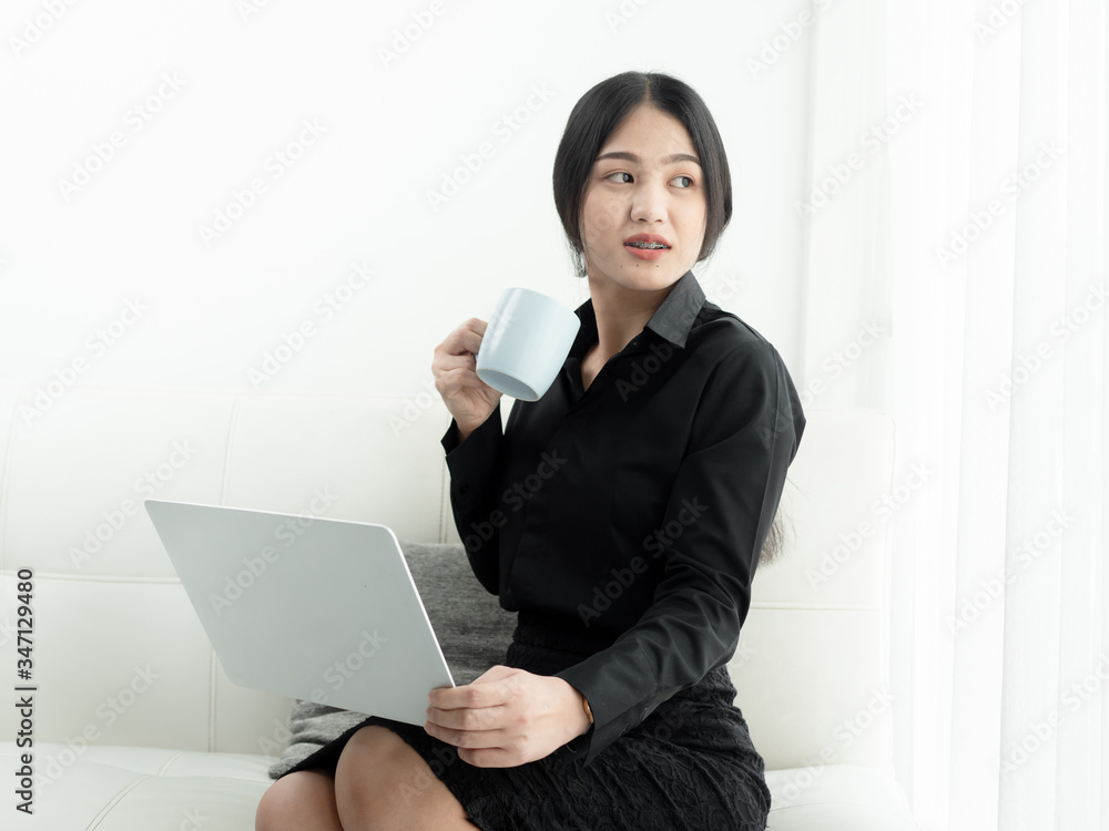 Asian woman in blank using laptop and drinks coffee sitting on sofa at home, quarantine concept. Asian woman in blank using laptop and drinks coffee sitting on sofa at home, quarantine concept.