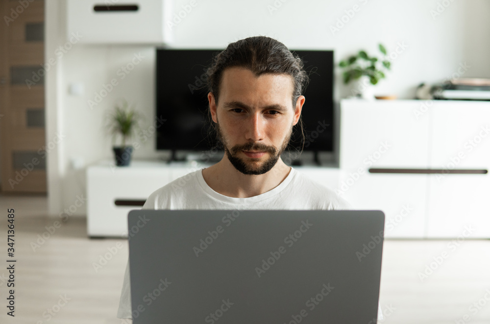 Man with beard, working at home on project with a laptop in front of him or speaking with a friends or business partners or clients via webcam and sitting on a floor. Freelancer working from home. Man with beard, working at home on project with a laptop in front of him or speaking with a friends or business partners or clients via webcam and sitting on a floor. Freelancer working from home.