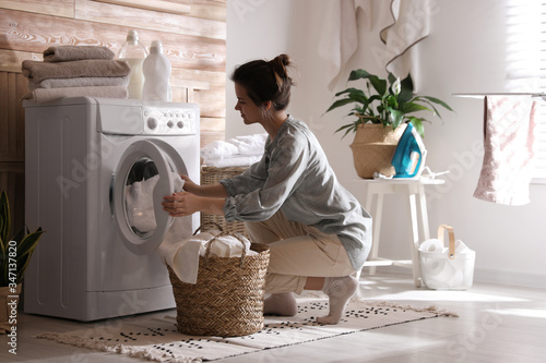 Foto Young woman taking laundry out of washing machine at home