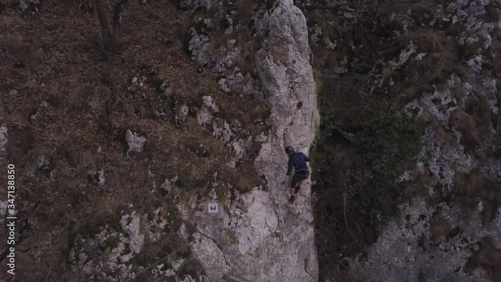 Climber steps off swinging bridge and begins to scale sheer rock wall. Man climbing cliff face on Via Ferrata - Casa Zmeului in Romania. Mountaineering excursion in Eastern Europe. Climber steps off swinging bridge and begins to scale sheer rock wall. Man climbing cliff face on Via Ferrata - Casa Zmeului in Romania. Mountaineering excursion in Eastern Europe.