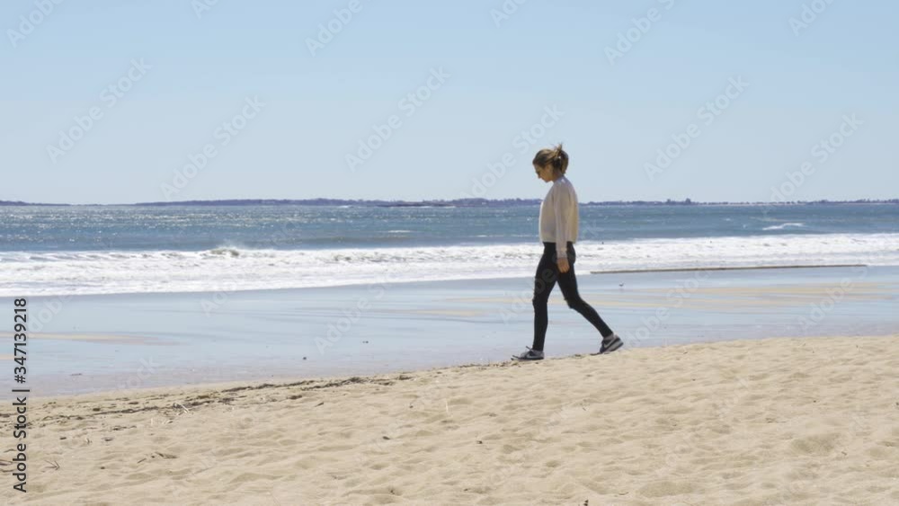 Attractive girl walking alone on a sandy beach during sunny day, relaxing moment Attractive girl walking alone on a sandy beach during sunny day, relaxing moment