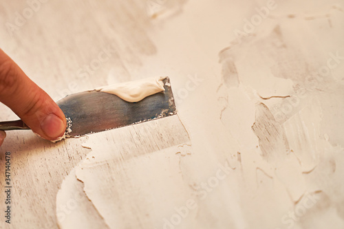 a small spatula applies putty to the wooden surface to create a structural background