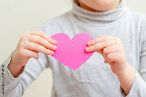 Closeup of pink paper heart in hands of child. Pink heart in child's hands.