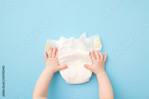 Baby hands touching white diaper on light blue table background. Pastel color. Closeup. Point of view shot. Top down view. photo