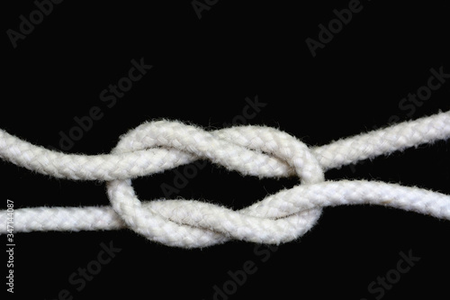 A white rope tied with granny knot on black background. © Siwapot Narukietmont