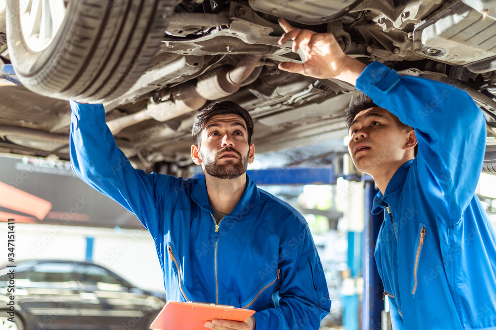 Two professional look technician inspecting car underbody and