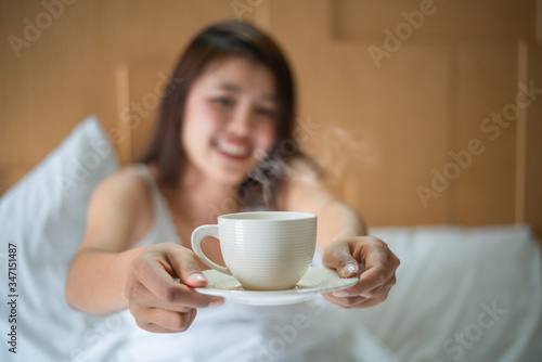 Asian cute woman drink coffee as breakfast on bed in morning after getting up. Relaxing concept. soft focus, selective focus.
