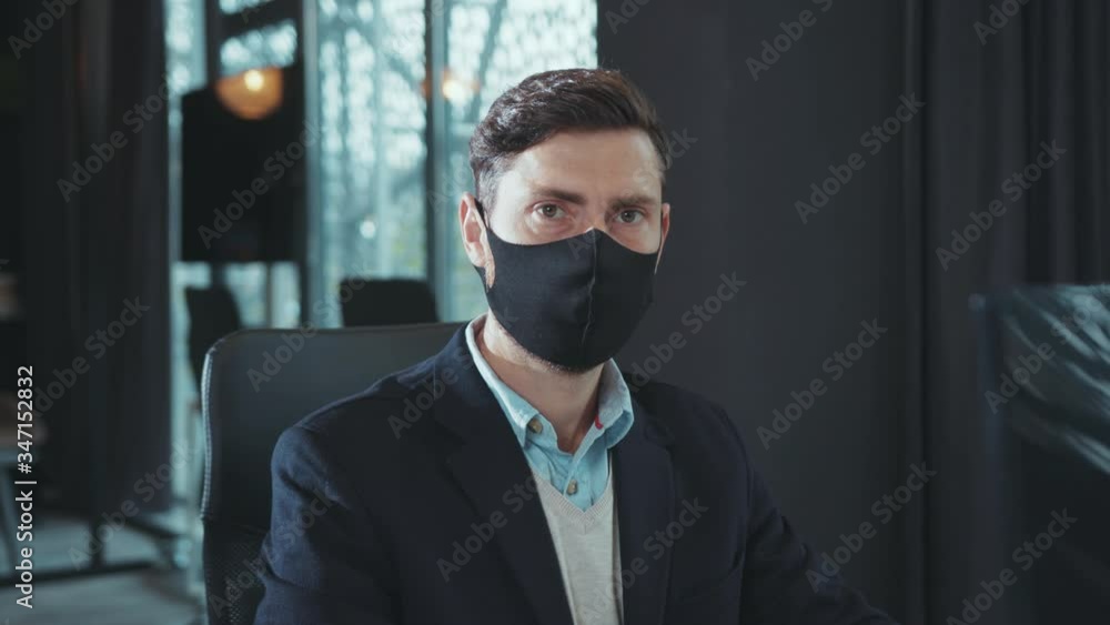 Young man wear mask work use computer look at camera serious in modern office business office worker epidemic hygienic protection businessman pandemic crisis keyboard coronavirus slow motion Young man wear mask work use computer look at camera serious in modern office business office worker epidemic hygienic protection businessman pandemic crisis keyboard coronavirus slow motion