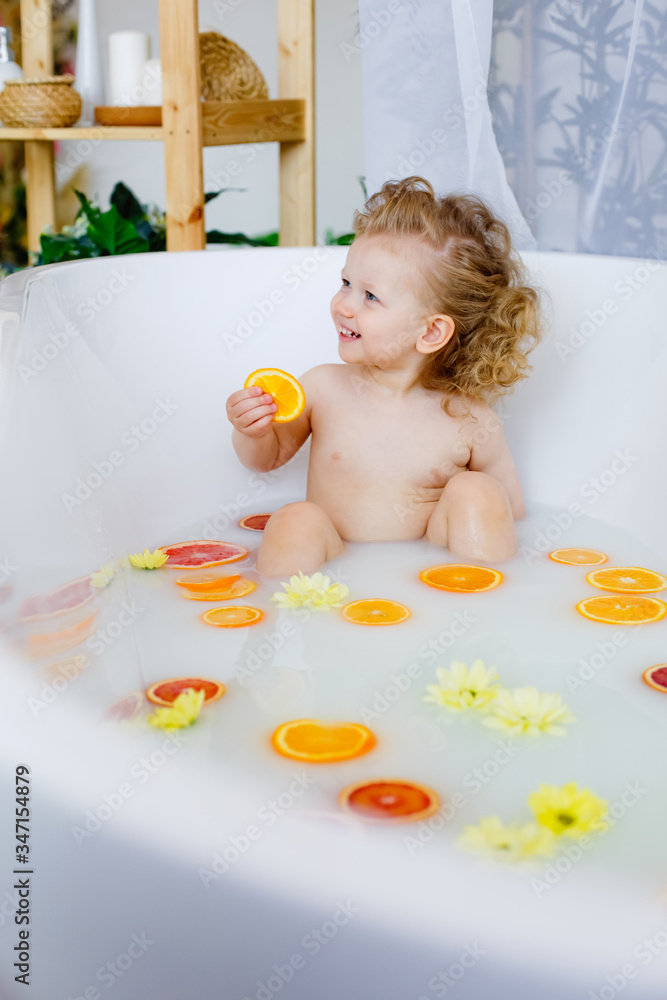 Child on the milk bath with flowersa little girl with curly hair in a milk bath with yellow flowers and orange oranges, red grapefruits. Child on the milk bath with flowersa little girl with curly hair in a milk bath with yellow flowers and orange oranges, red grapefruits.