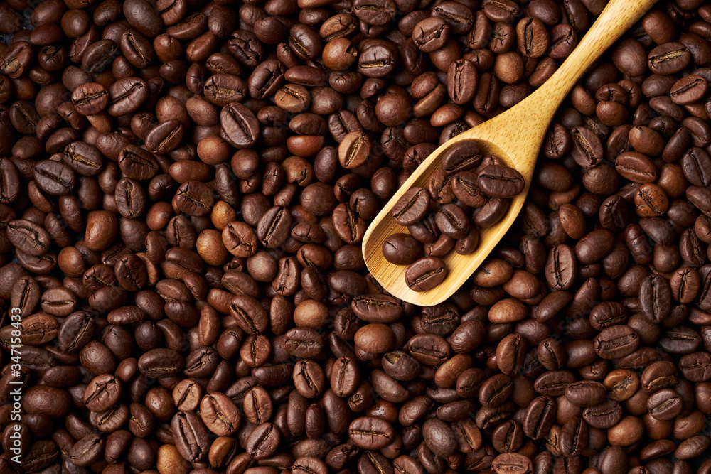Fototapeta premium Wooden spoon on a heap of roasted whole coffee beans
