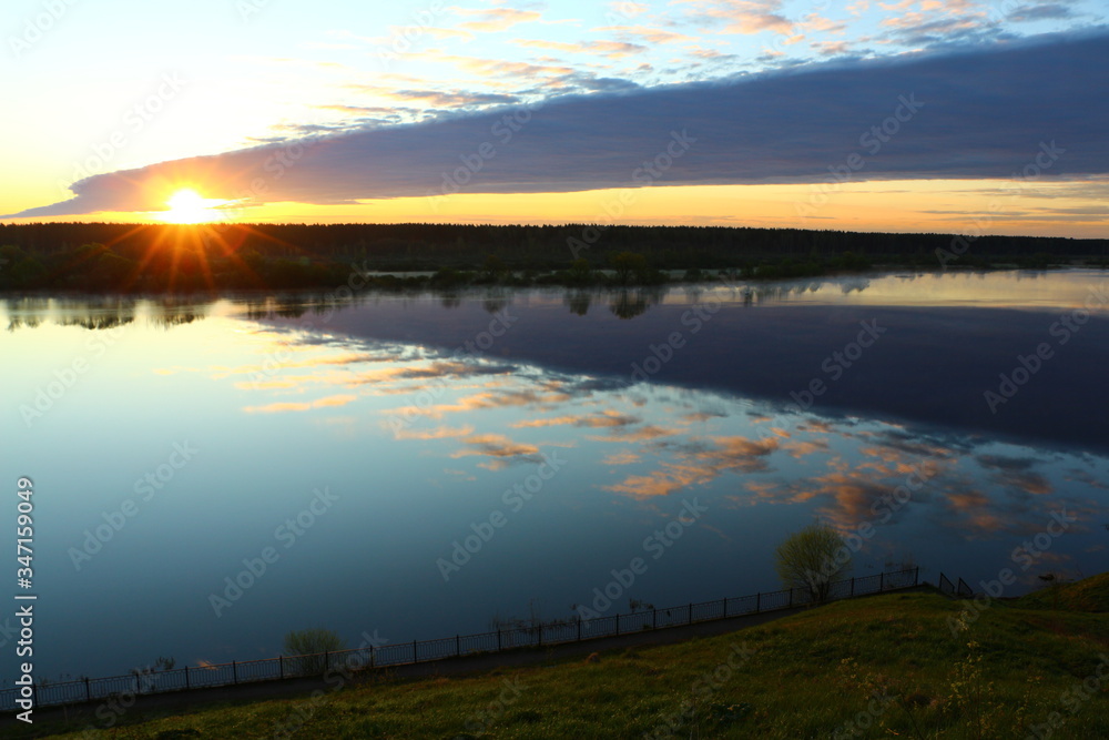 Picturesque landscape at dawn.A look from the high Bank at the hot sun with rays that lit up the sky and the blue river with Golden luminous clouds reflected on the surface of the water.Russia