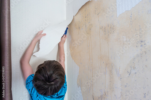 A young boy helps strip old wallpaper as the first stage of redecorating the room. photo