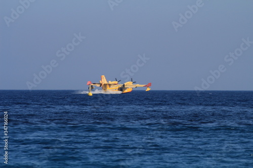 A canadair and a helicopter collect water and fly to the mountains to put out a big fire in Liguria.