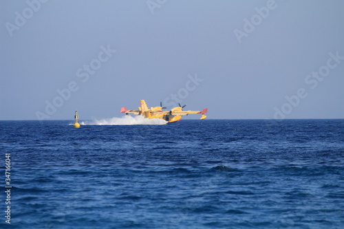 A canadair and a helicopter collect water and fly to the mountains to put out a big fire in Liguria.