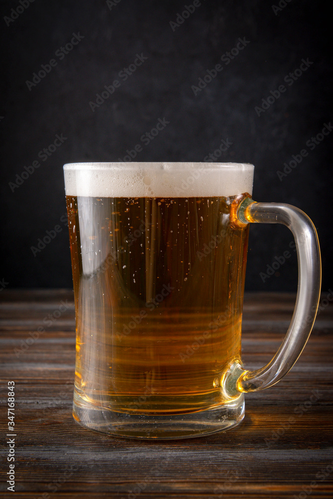 glass of barley beer with foam on a dark wooden background, alcoholic beverage