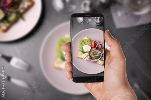 Blogger taking picture of delicious sandwich with ham at table, closeup. Food photography photo