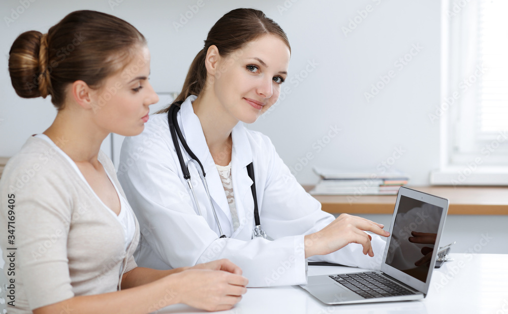 Doctor and patient are sitting and discussing health examination results while using laptop computer. Health care, medicine and good news concepts Doctor and patient are sitting and discussing health examination results while using laptop computer. Health care, medicine and good news concepts