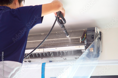 The technicians are cleaning the air conditioner by spraying water. Hand and water spray are cleaning the air conditioner on with white wall background. photo